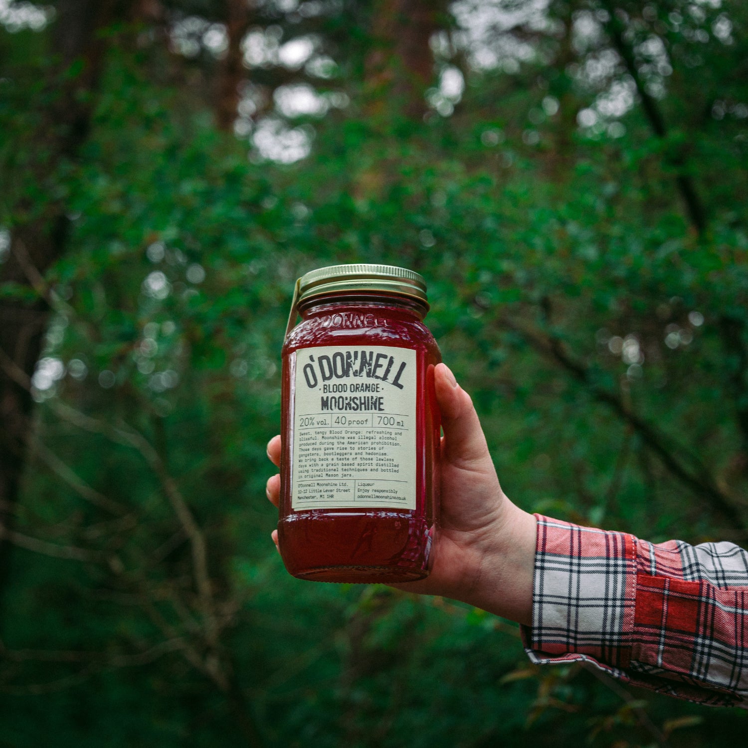 Hand holding O'Donnell Moonshine Blood Orange in woods